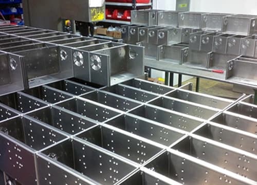 Rows of precisely fabricated sheet metal enclosures with perforations, arranged in an industrial workshop.